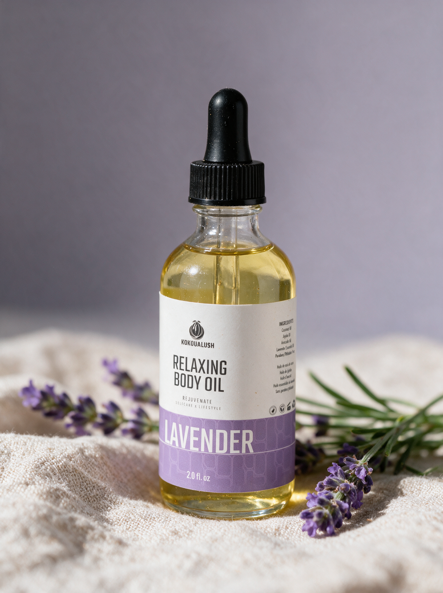 Kokoualush Lavender Relaxing Body Oil dropper bottle on oatmeal linen with fresh lavender
