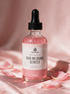 Kokoualush Rub Mi Dung Gently pink shimmer Body Glow Oil dropper bottle on blush silk with rose petals