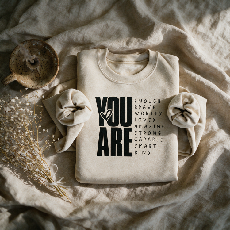Kokoualush You Are Enough sand crewneck folded flat-lay on linen with dried florals and ceramic mug