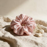 Kokoualush blush pink silk satin scrunchie resting on oatmeal linen with dried baby&