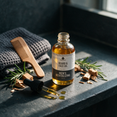 How to use Kokoualush beard oil: dropper dispensing on a dark slate shelf with comb, towel and rosemary