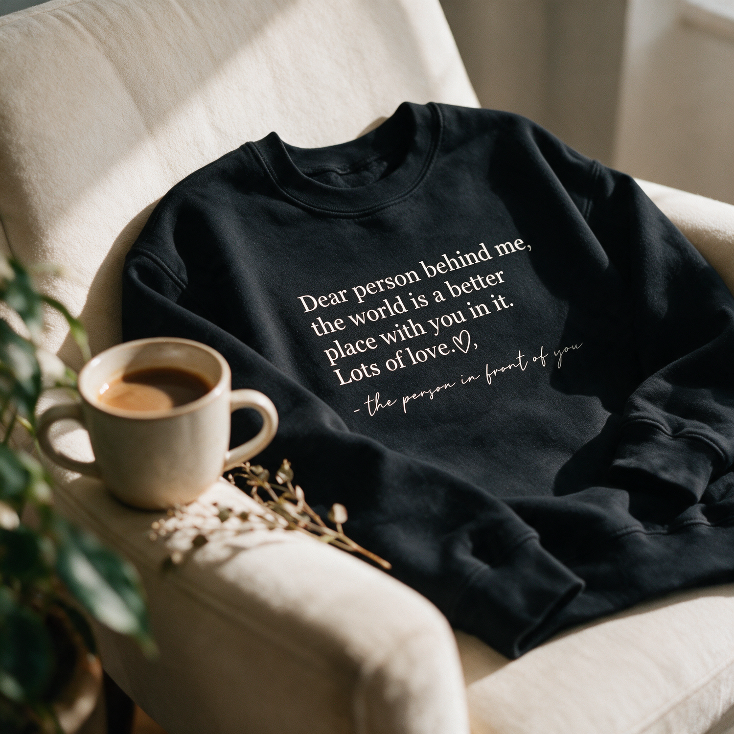 Be Kind black crewneck draped over a chair in warm cozy light