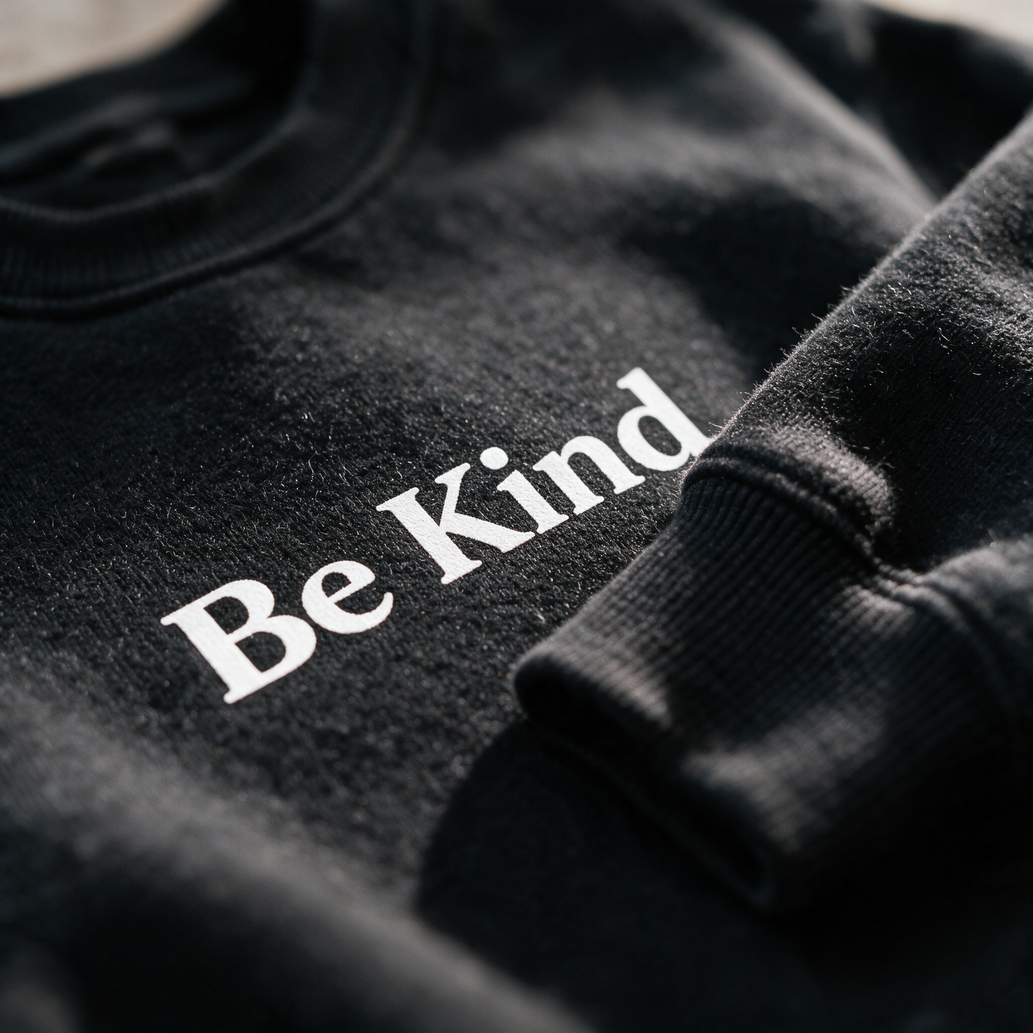 Macro of the black crewneck fleece and Be Kind print detail