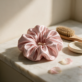 Blush pink silk scrunchie on a marble vanity with rose petals